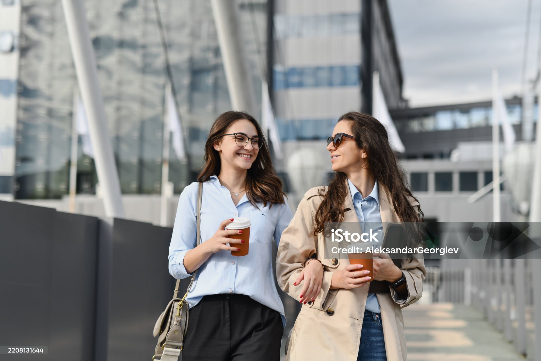 Joyful Females Holding Each Other Under Arms With Cups of Coffee and Chatting
